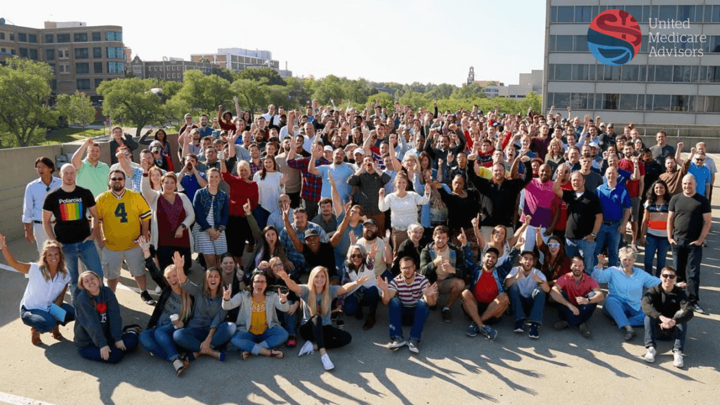 All of our United Medicare Advisors agents posing for a group photo on a sunny day surrounded by trees and buildings