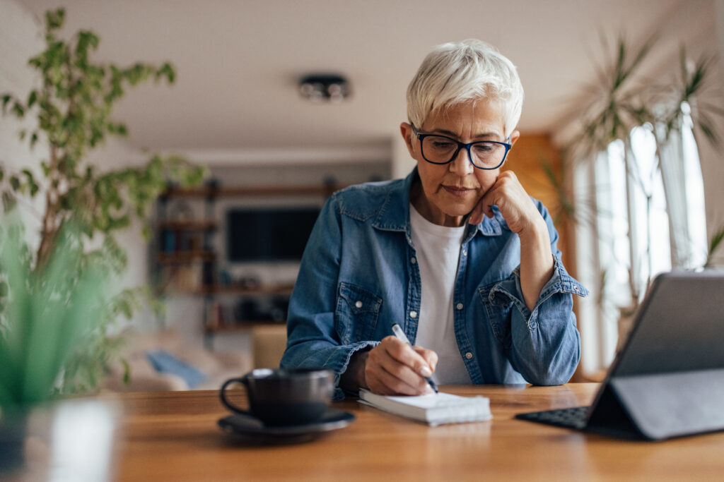 Mature woman, taking notes during a free online course on her tablet