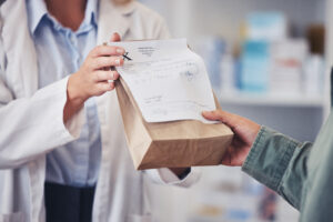 Pharmacist hands prescription medicine to customer in paper bag.