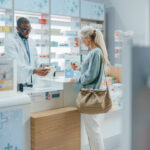 Pharmacy Drugstore Checkout Counter: Professional Black Pharmacist Provides Service, Sells Medicine to Senior Woman Customer. She is Paying with Use of Contactless Payment Credit Card and Part D coverage
