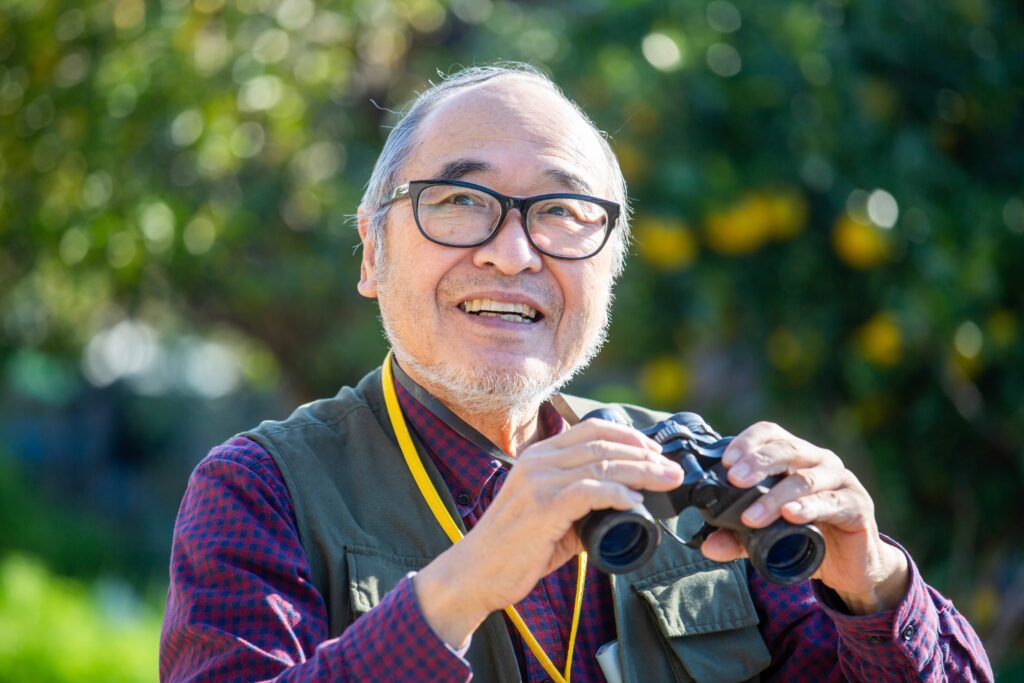 Older Asian man holding binoculars outside, getting started birdwatching for beginners