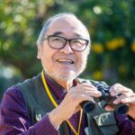 Older Asian man holding binoculars outside, getting started birdwatching for beginners