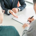 An older couple signing paperwork with an advisor, planning ahead for expenses for loved ones, like final expense insurance.