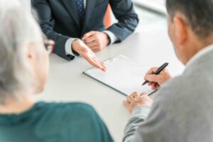 An older couple signing paperwork with an advisor, planning ahead for expenses for loved ones, like final expense insurance.