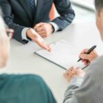 An older couple signing paperwork with an advisor, planning ahead for expenses for loved ones, like final expense insurance.