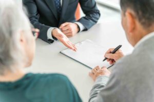 An older couple signing paperwork with an advisor, planning ahead for expenses for loved ones, like final expense insurance.