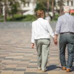 Senior adults walking in a park holding hands. One senior is using a cane.