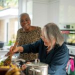 Two senior women preparing meal in kitchen, a diet for stronger bones can be easier to manage with cooking meals at home.