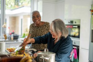 Two senior women preparing meal in kitchen, a diet for stronger bones can be easier to manage with cooking meals at home.