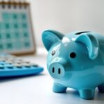 Blue piggy bank sits on white surface with blue calculator, calendar in background. Concept for what to know about how to change Medicare Supplement plans.