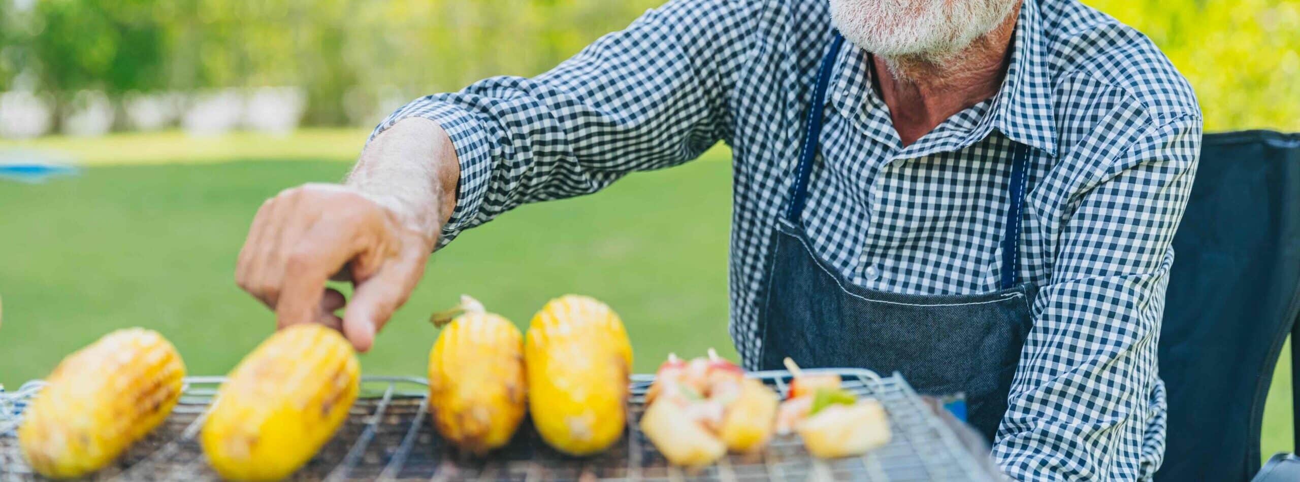 Senior man relax grilling corn and other late summer produce outdoors on the grill in a backyard
