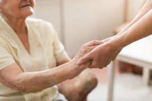 A palliative care specialist holds the hand of a senior patient sitting in a wheelchair.