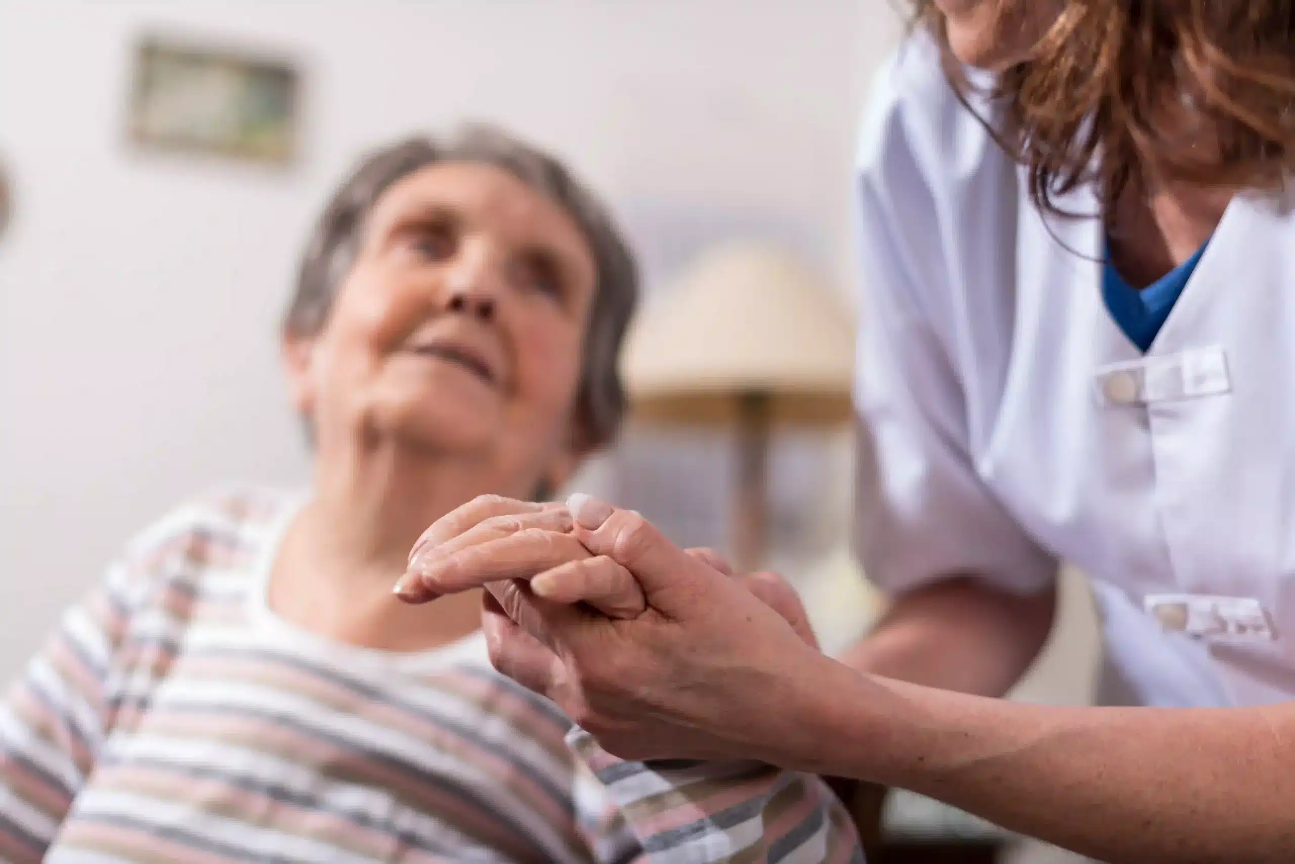 A skilled nursing aid holds the hand of an elderly woman in a nursing home