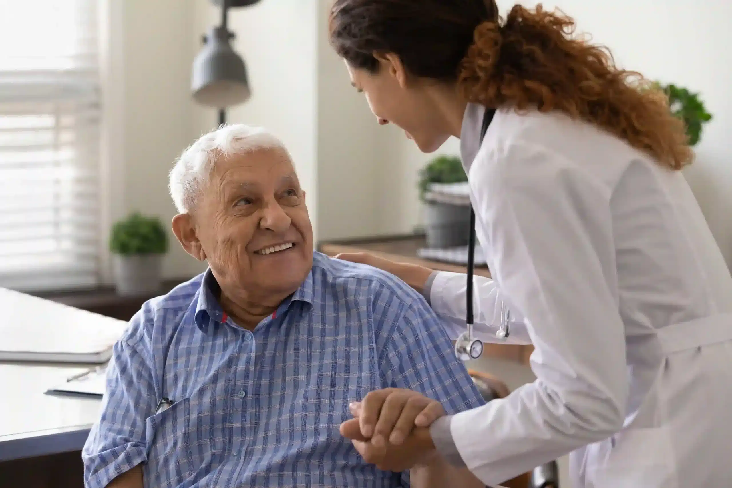 A senior man is being helped by the hand of a female physician in a doctor’s office